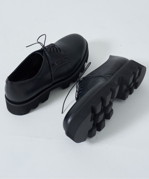 A pair of black leather plain-toe dress shoes with chunky lug soles, shown angled with one shoe displaying the sole.