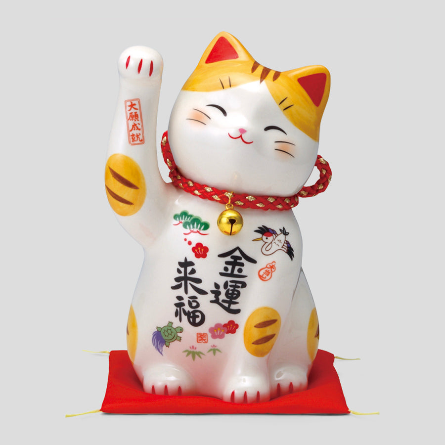 Painted ceramic maneki-neko coin bank with raised left paw, red collar and bell, sitting on a red cushion.