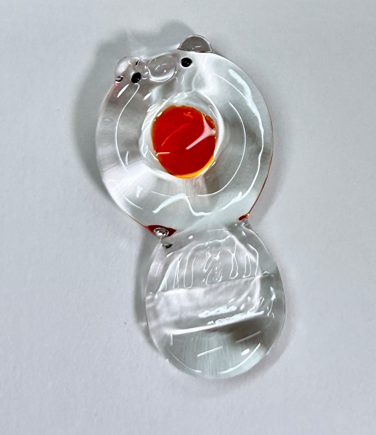A clear glass 'Palette-kun' ink saucer and pen rest shaped like a small character with a round well holding red ink on a white background.