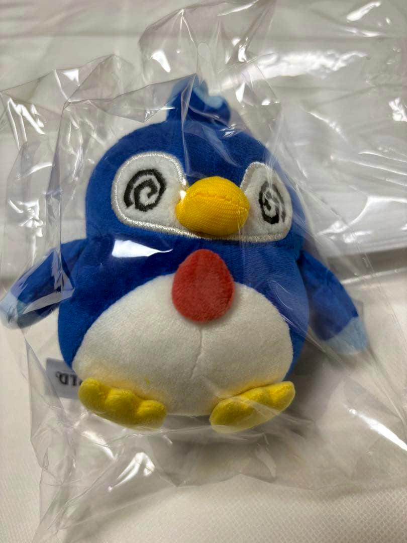 Front view of the TGS2026 Palworld Pentama plush with spiral eyes, yellow beak and feet, and a white belly inside clear plastic packaging.