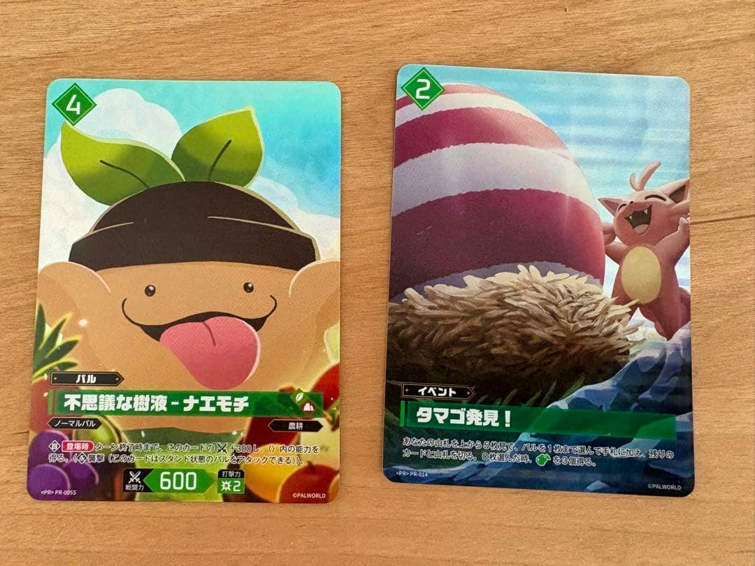 Photo of two Palworld promo trading cards on a wooden surface, with the '不思議な樹液-ナエモチ' card visible on the left.