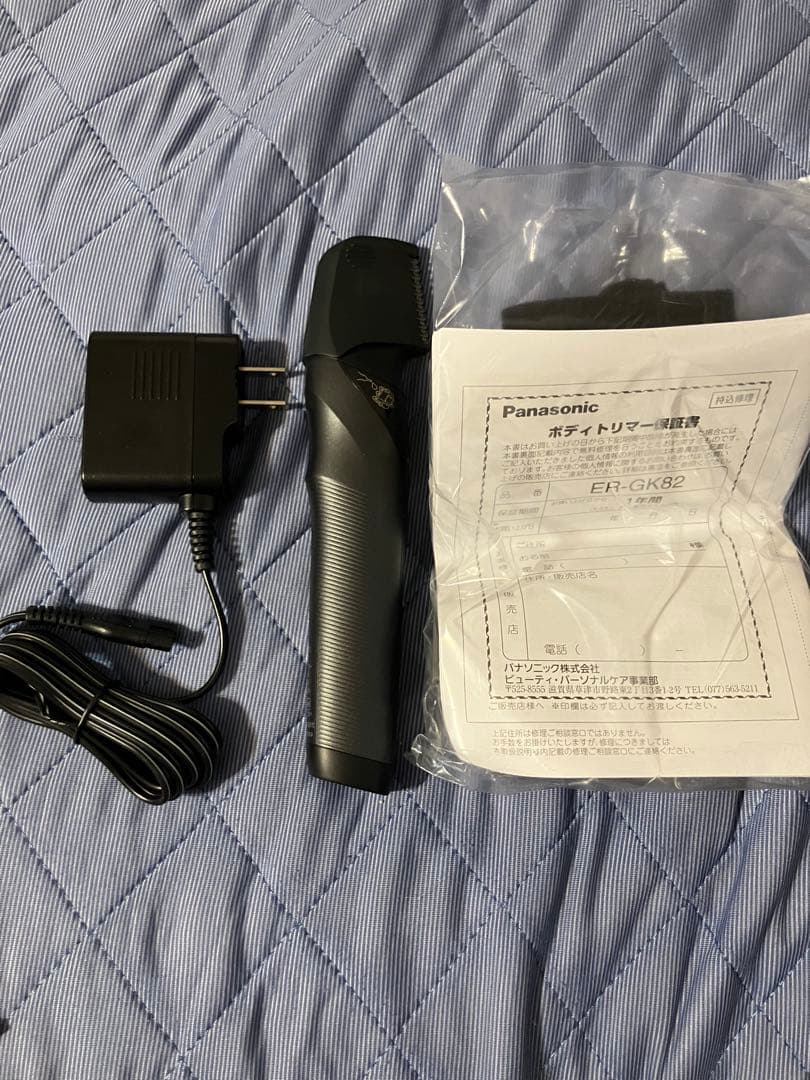Panasonic body trimmer ER-GK82 with its charger and instruction manual laid on a quilted surface.