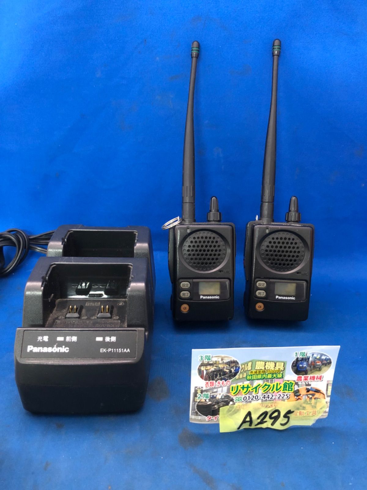Two Panasonic EK-3299C handheld transceivers with antennas and a two-unit charging stand placed on a blue background.