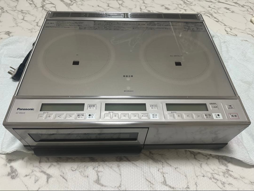 Top-front view of a Panasonic KZ-KM22E induction cooktop showing two circular cooking zones, the control panel, and a front drawer.