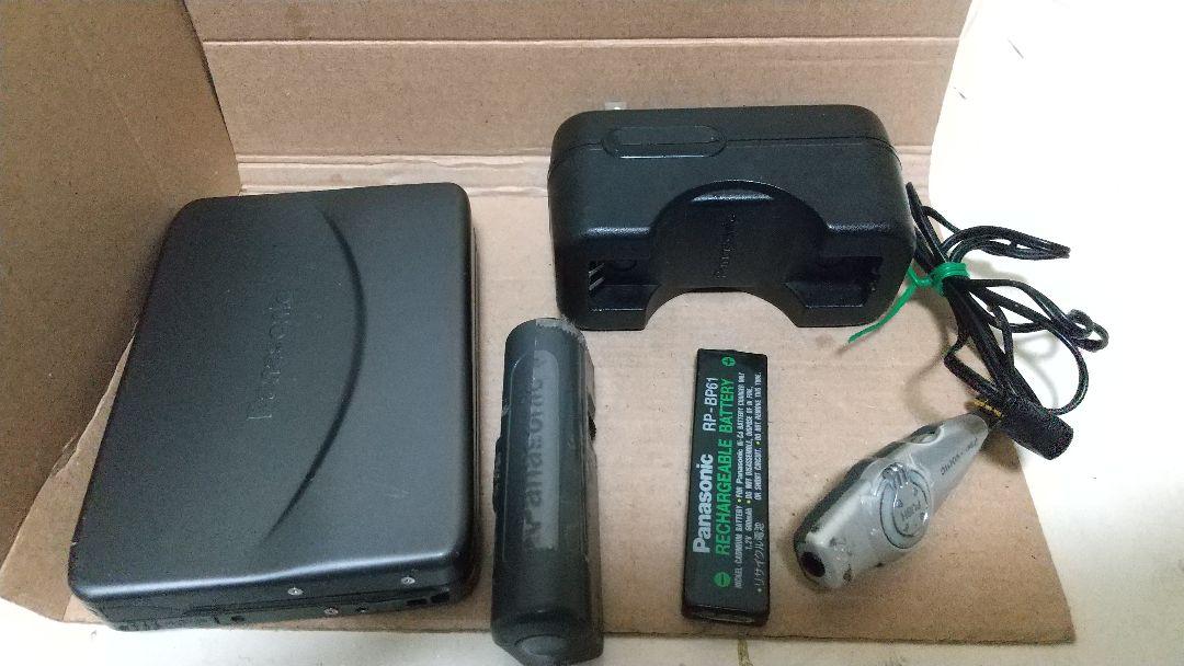 Panasonic cassette player and accessories (battery, charger, earbud) arranged inside a cardboard box.