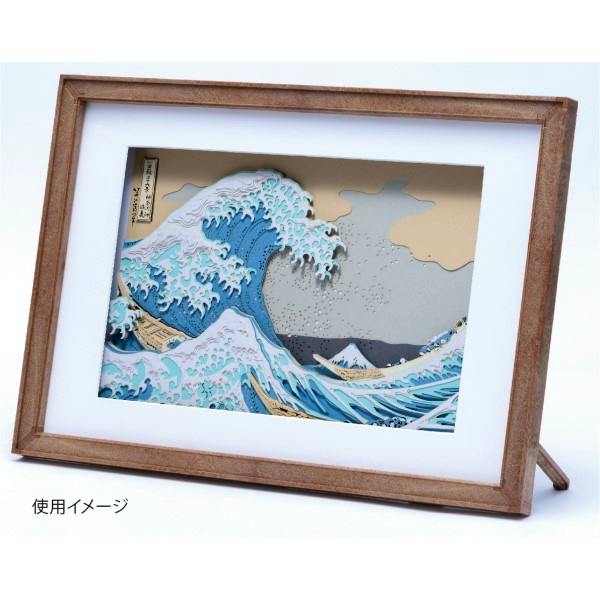 Wooden display frame holding a layered paper shadow art print of a wave scene, shown angled on its stand.