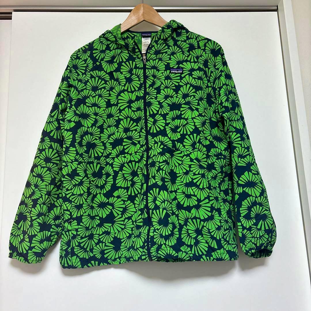 Front view of a Patagonia kids' nylon windbreaker (XL) with a green floral-like pattern hanging on a wooden hanger.