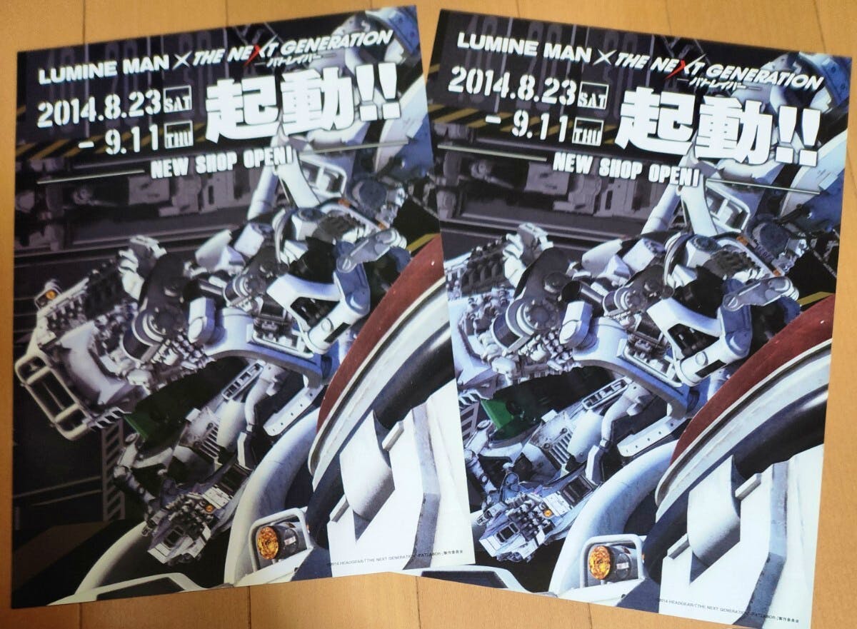 Two A4 promotional flyers for the “パトレイバー” LUMINE MAN tie-up laid side by side on a wooden floor.
