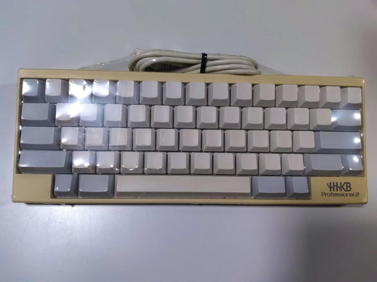 Top-down photo of a compact HHKB Professional 2 PC keyboard with white and gray keycaps wrapped in plastic.