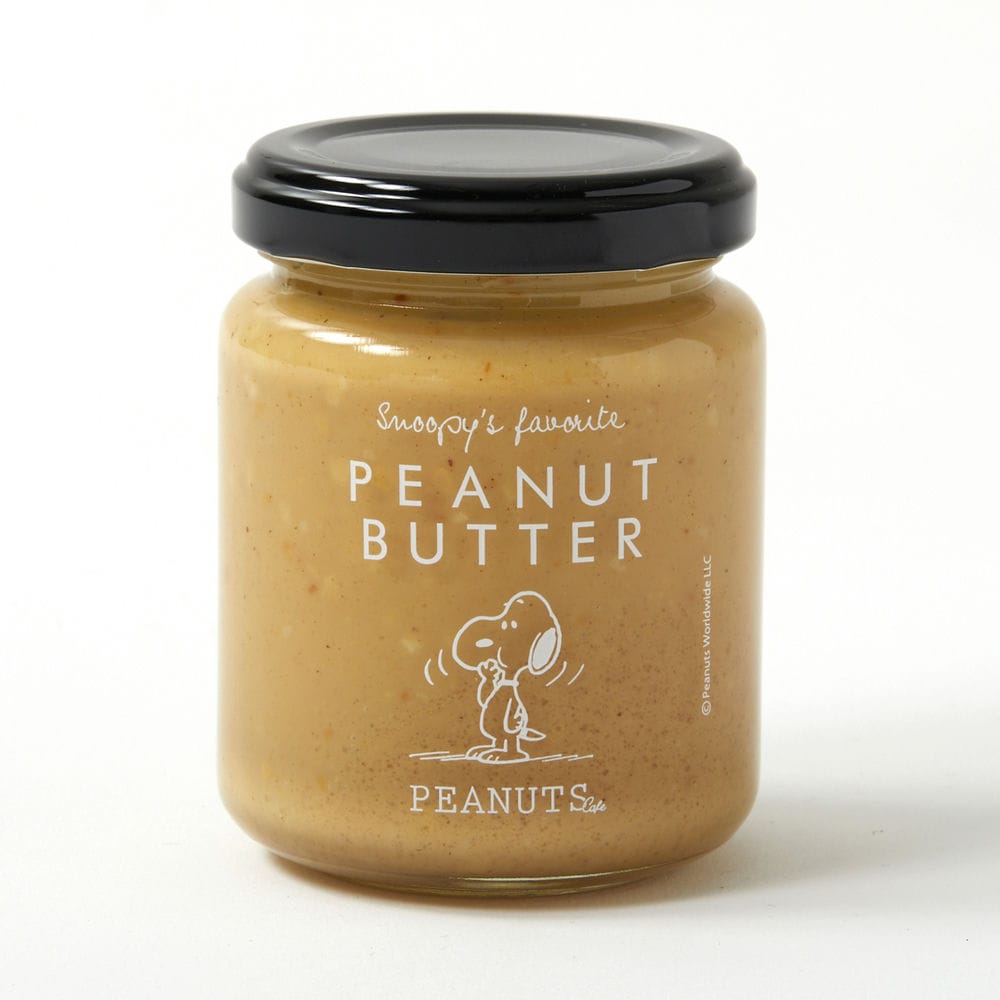 A glass jar of peanut butter with a black lid and a white 'PEANUT BUTTER' Snoopy label.