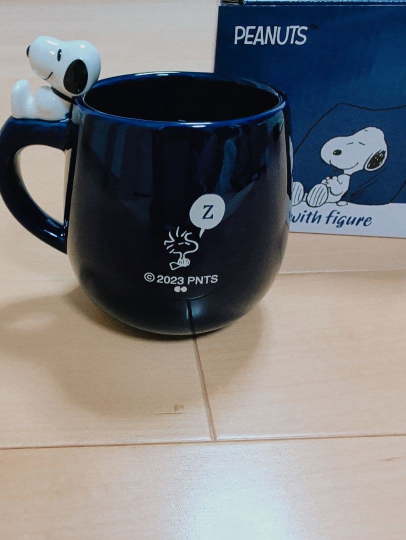Navy ceramic mug with a Snoopy figure attached to the handle, shown with the Peanuts box behind it.