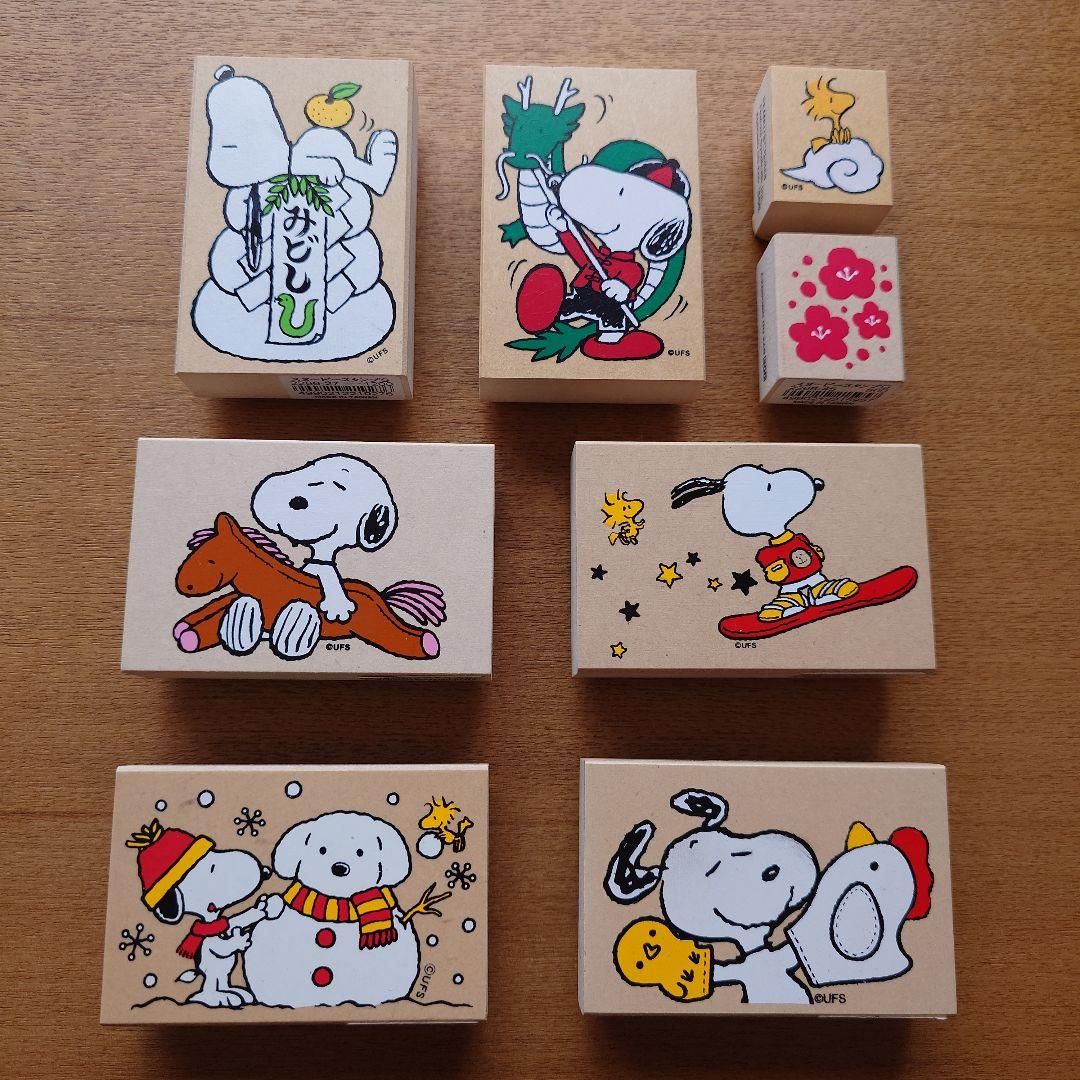 Eight wooden PEANUTS (Snoopy) stamps with printed character illustrations arranged on a wooden surface.