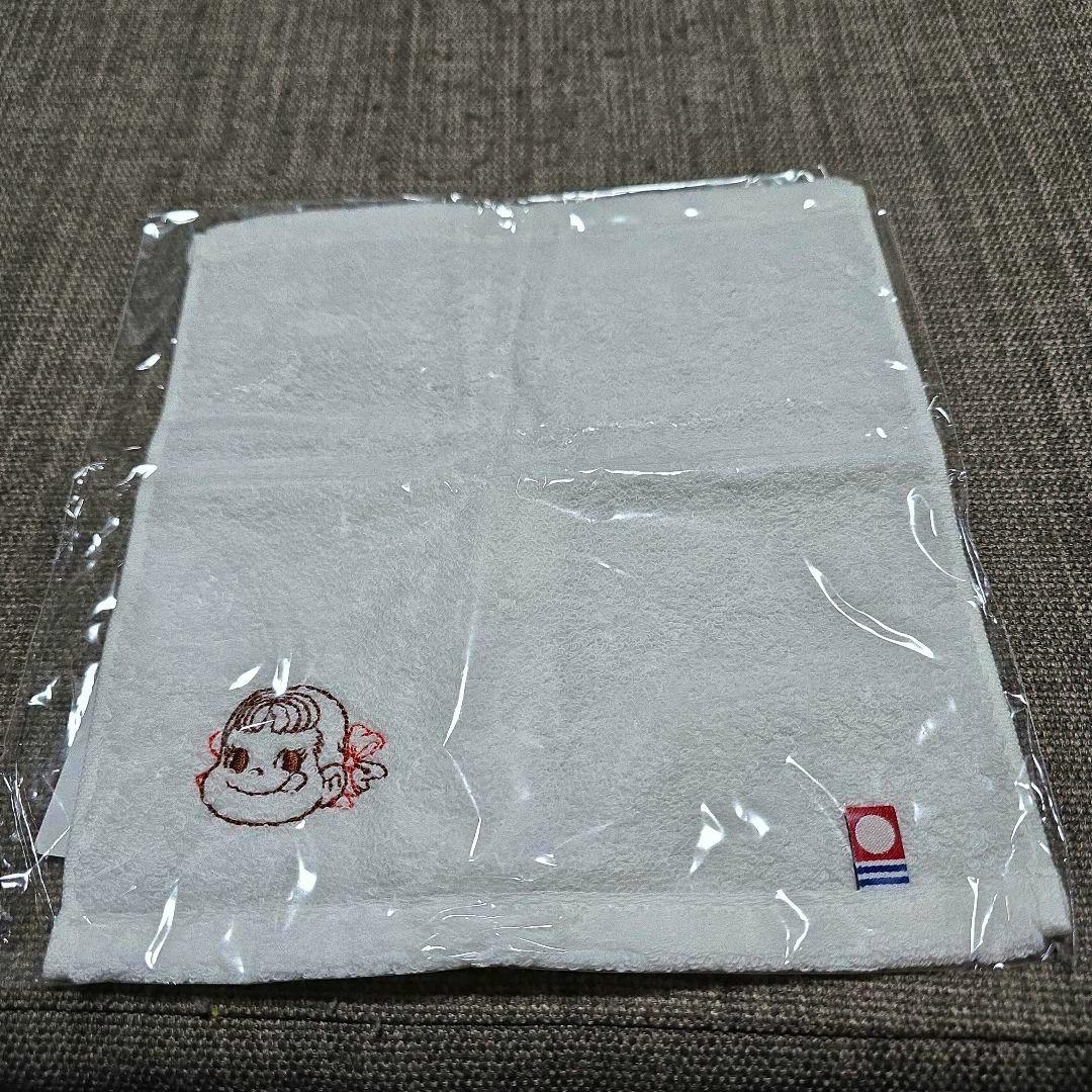 White cotton mini hand towel with Peko-chan character embroidery and a small logo, shown in clear plastic packaging on a fabric surface.