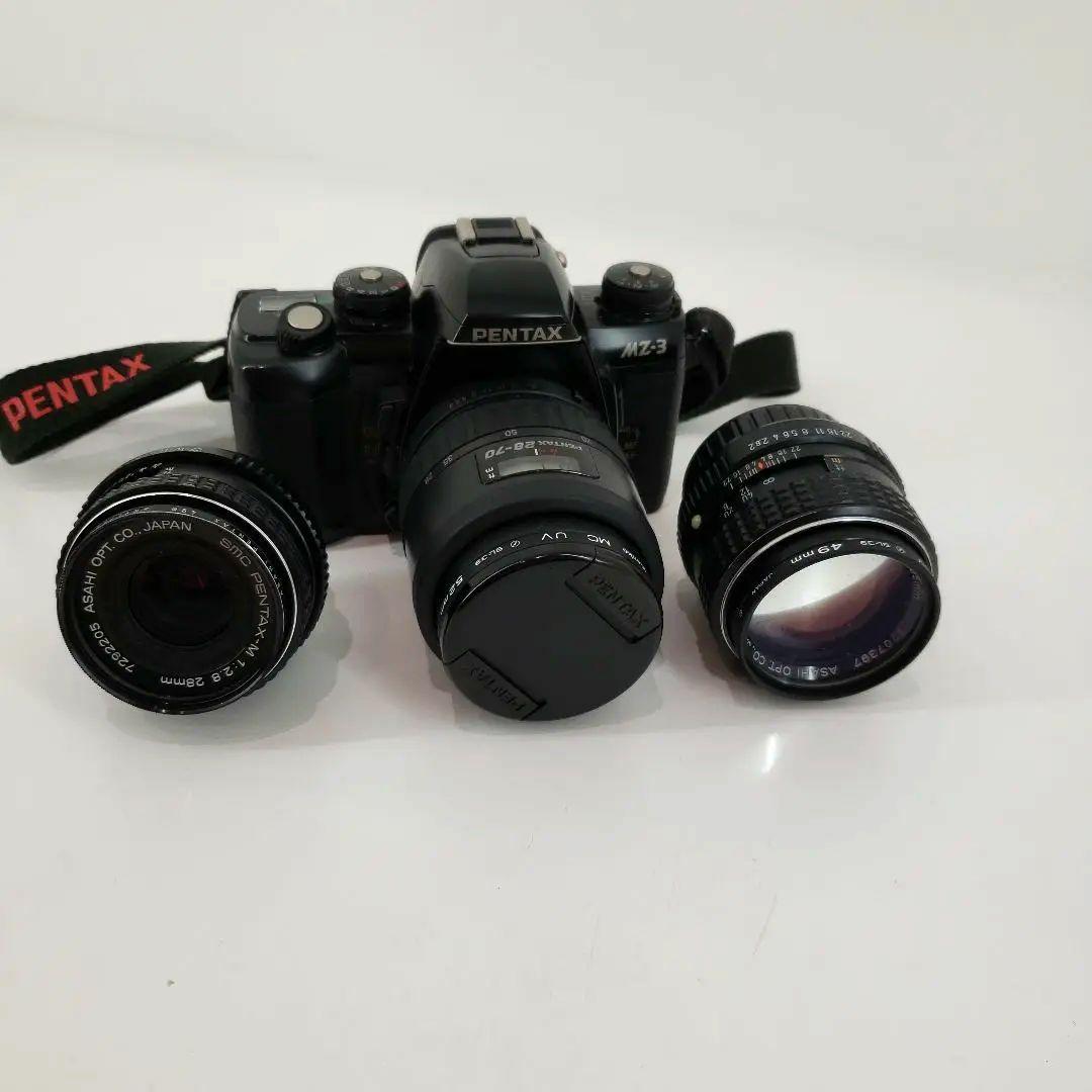 Pentax MZ-3 film camera body with two detached prime lenses arranged on a white surface.