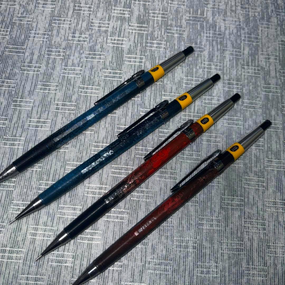 Four Pentel PG5 mechanical pencils with wrap-painted barrels in different colors arranged on a patterned fabric background.