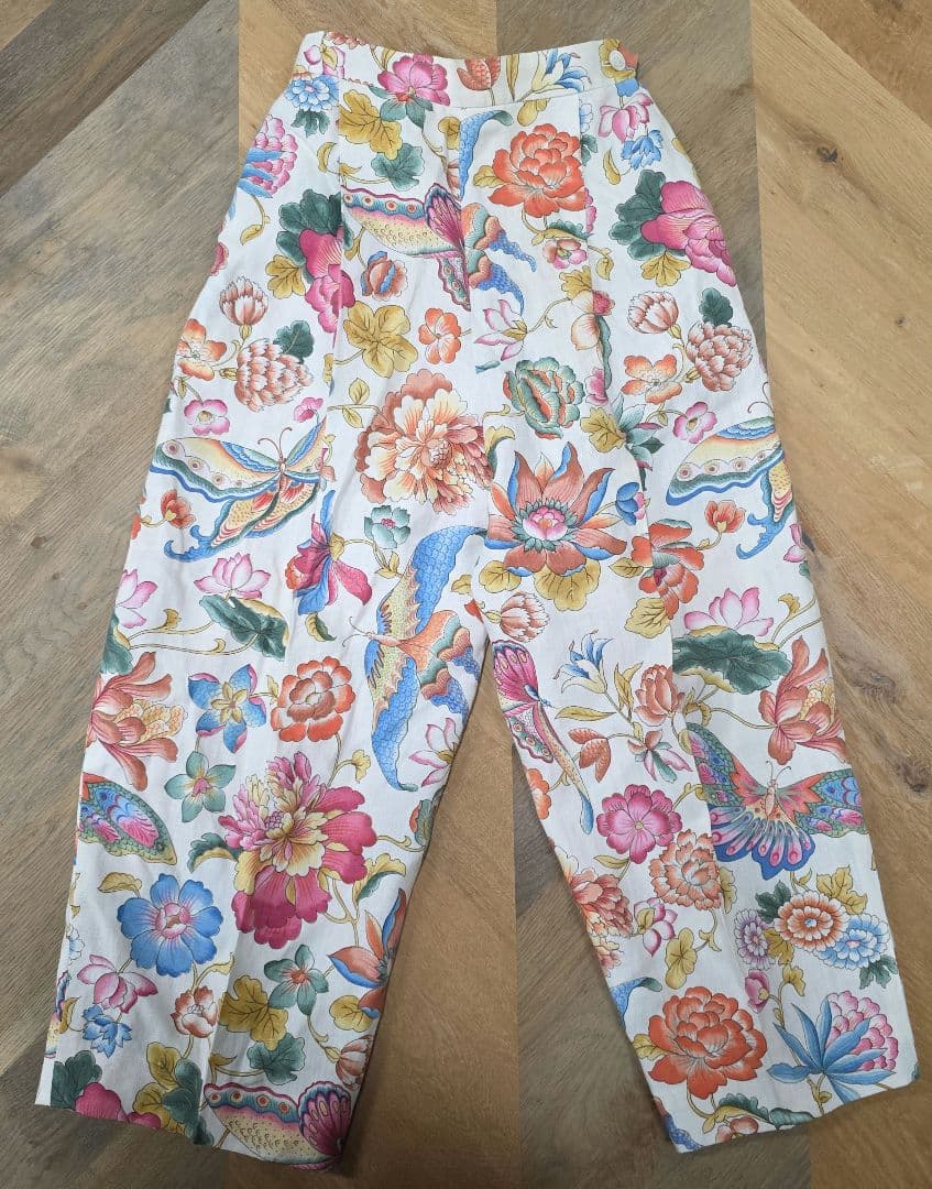 Flat-lay front view of women's linen pants with a colorful floral and bird pattern.