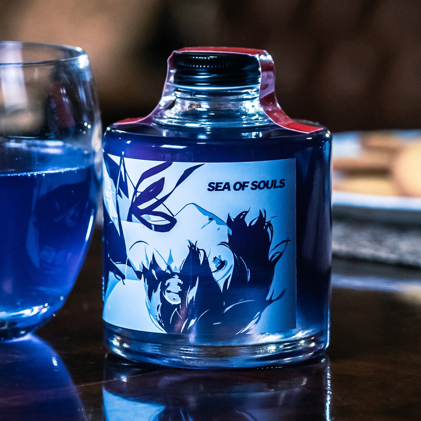 Bottle of Persona 3 Reload "Sea of Souls" cola base syrup with deep blue liquid shown beside a glass.