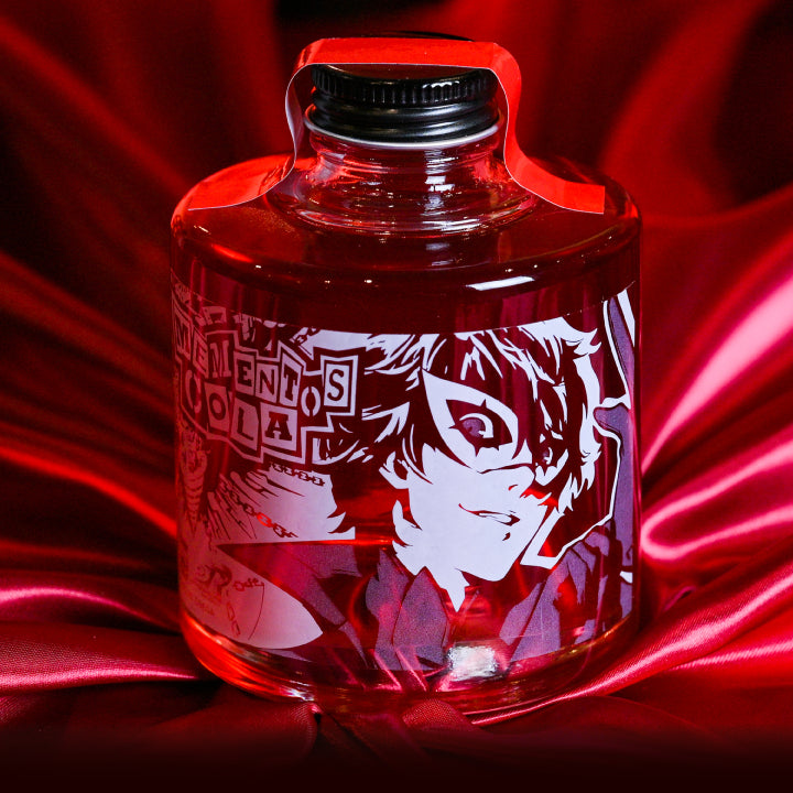 A clear bottle of Persona 5 “Mementos Cola” cola base syrup with character artwork on the label displayed on red fabric.