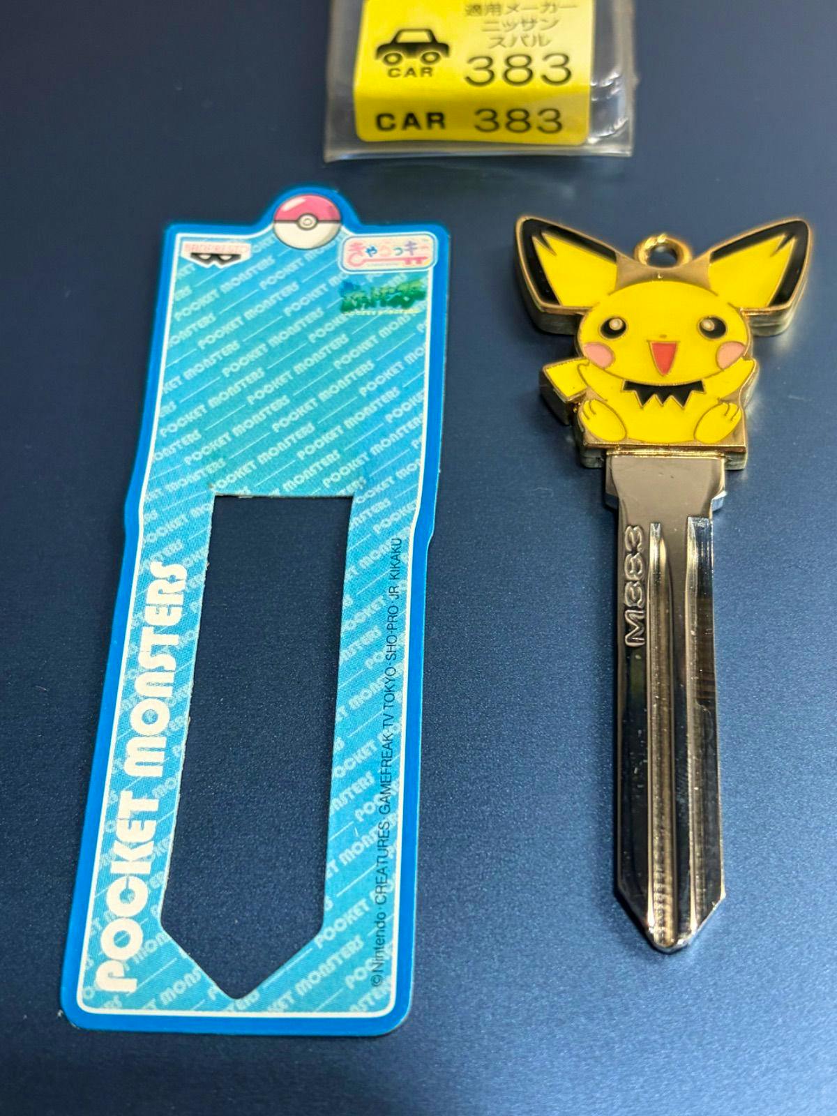 Metal car key cover showing a Pichu character head attached to an M383 car key blade beside a blue "Pocket Monsters" template.
