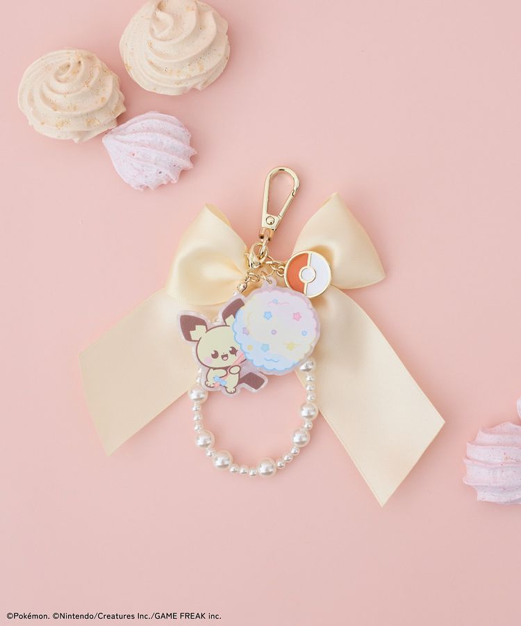 Cream ribbon charm with a Pichu character charm, a pearl-beaded loop, and a gold clasp on a pink background.