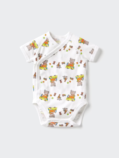 Flat-lay photo of a white short-sleeve children's bodysuit (front-opening) with an all-over illustration of a small bear driving a vehicle on a light gray background.