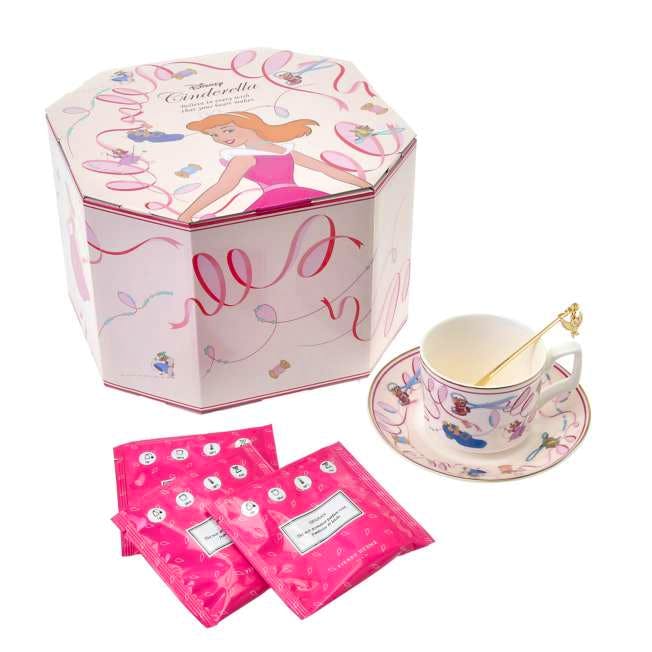 Pink Cinderella-themed teacup and saucer set shown with its decorative octagonal box, a gold spoon, and three pink tea sachets.