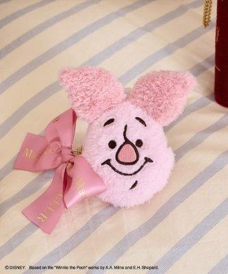 Plush pink Piglet face pouch charm with a pink ribbon bow and gold chain on a striped fabric background.