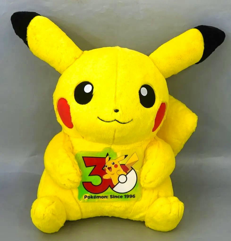 Yellow Pikachu plush (male form) sitting and holding a Pokémon 30th anniversary logo patch.