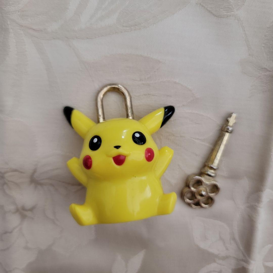 Yellow Pikachu-shaped padlock shown with its metal key on a light fabric background.