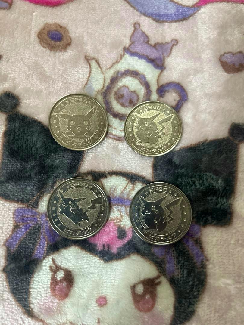 Four metal Pikachu Pokémon coins (medals) arranged on patterned fabric showing Pikachu faces.