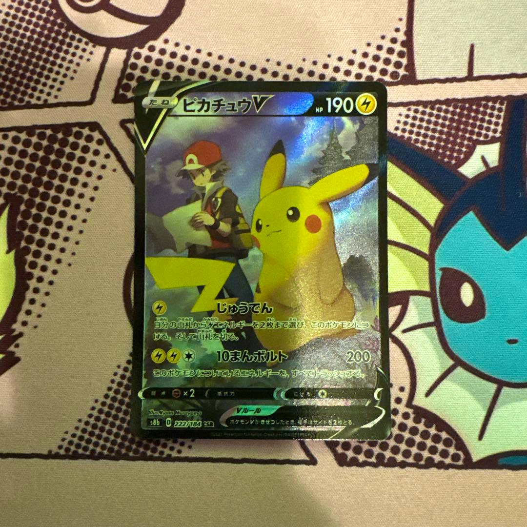 Photograph of the trading card ピカチュウV CSR S8b VMAXクライマックス 222/184 placed on a patterned playmat, showing the full holographic card.