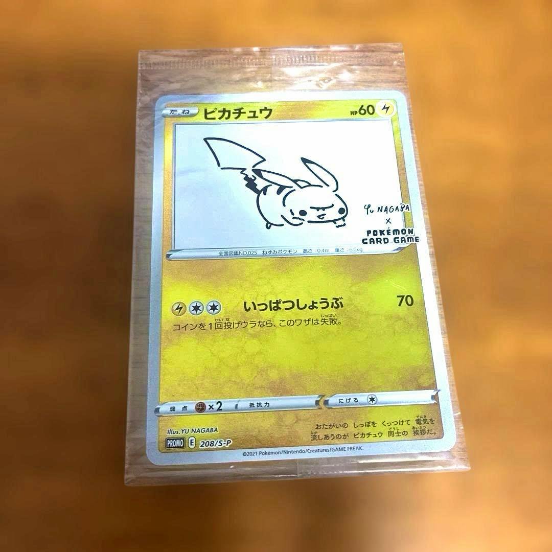 Front of the ピカチュウ YU NAGABA×ポケモンカードゲーム PROMO S-P trading card shown inside a clear protective sleeve on a wooden surface.
