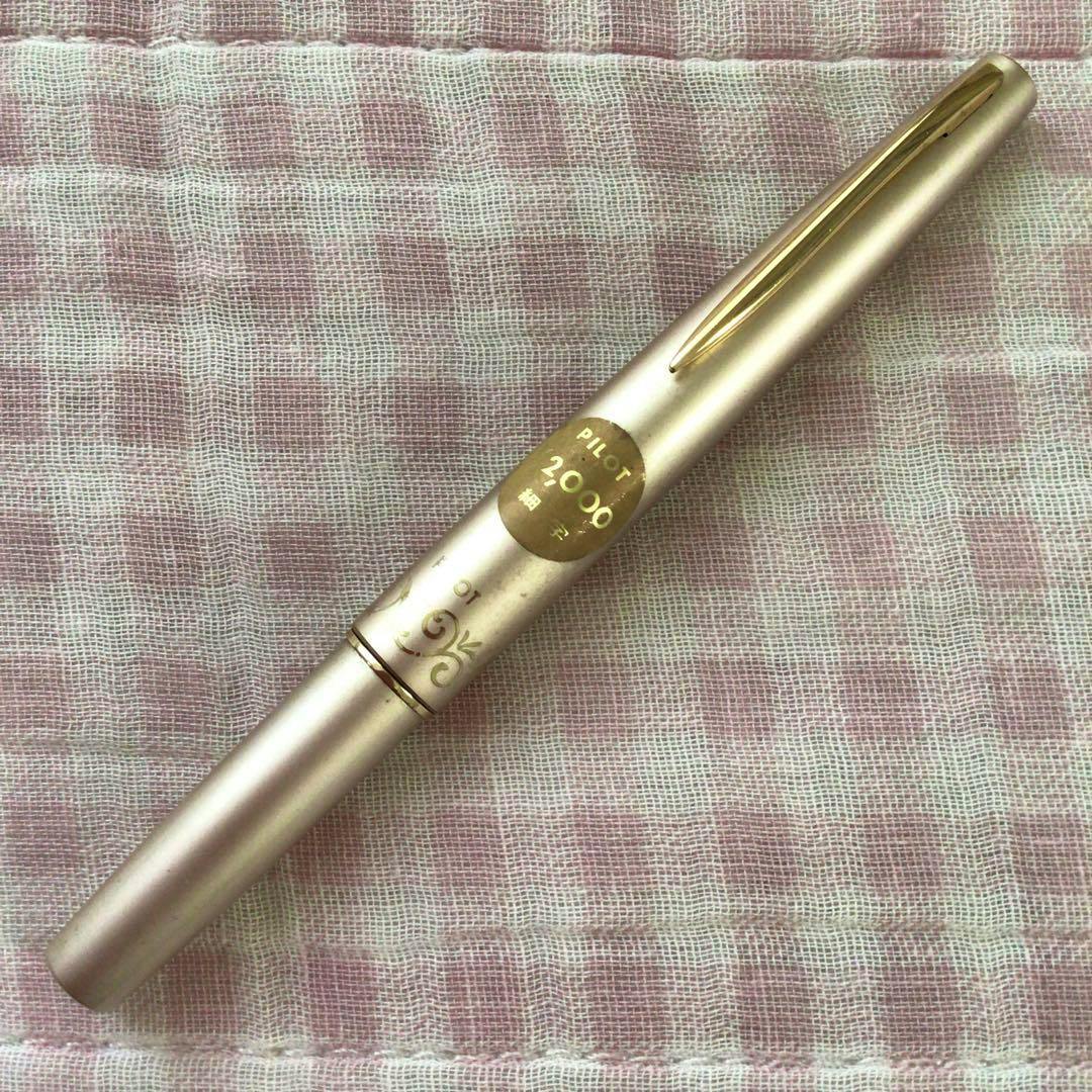 Closed Pilot 18K short fountain pen with cap on, showing a gold clip and round "PILOT 2000" sticker, placed on pink checked fabric.