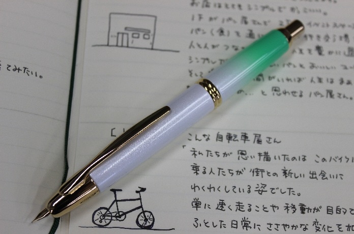 Photo of the Pilot Capless fountain pen in a green-to-white gradient resting on an open notebook.