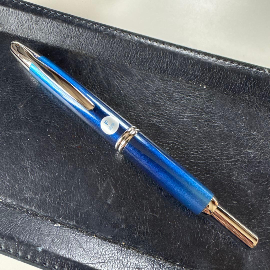 Blue Capless fountain pen with an F nib sticker resting capped on a black leather surface.