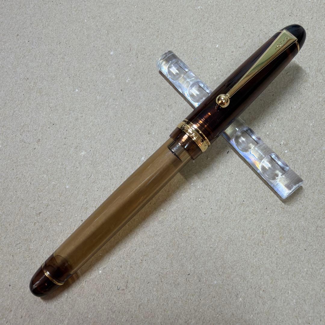 Clear brown Pilot Custom 74 fountain pen resting on a clear plastic pen stand on a light surface.