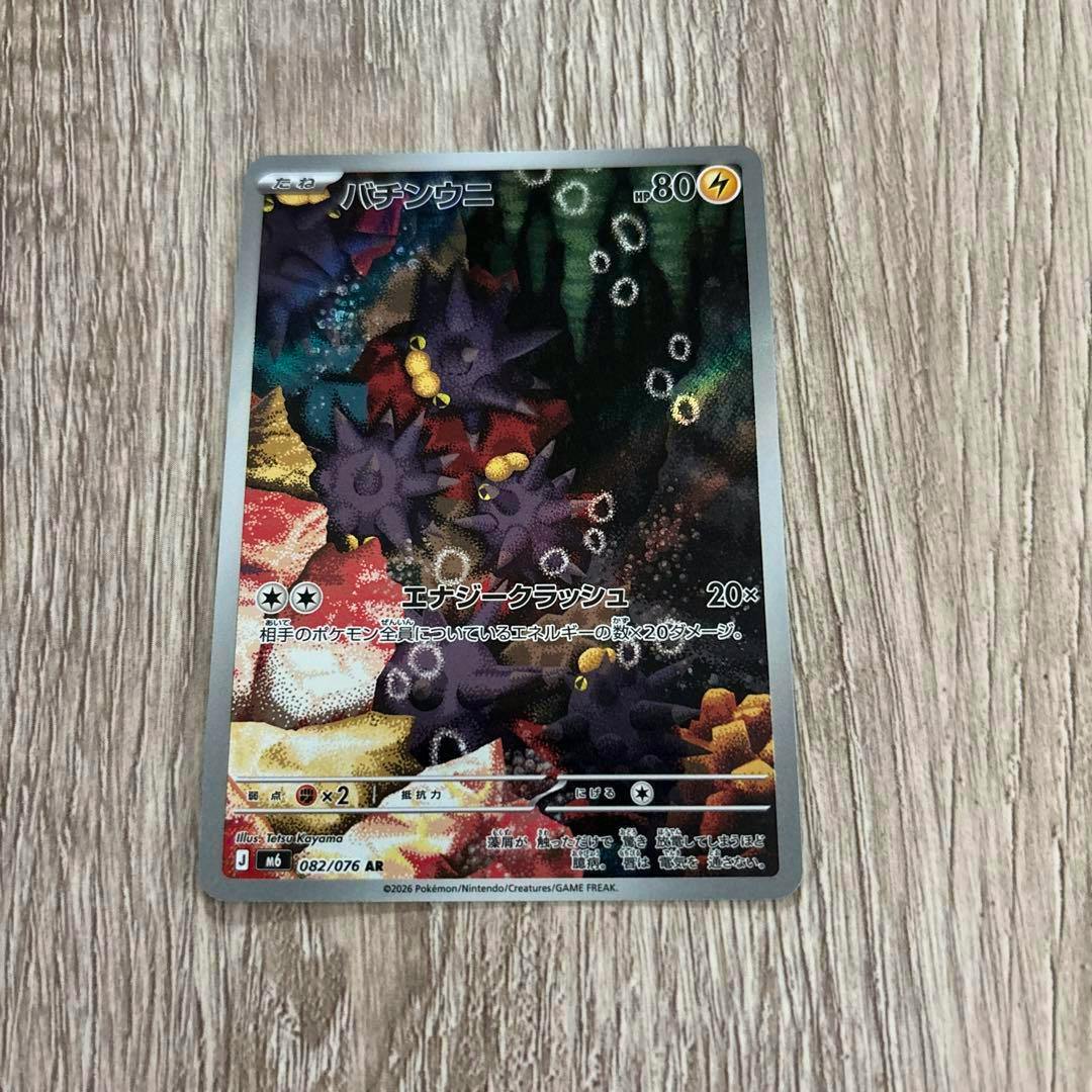Front of the バチンウニ trading card showing the card artwork, Japanese text, and set number 082/076 AR on a wood surface.