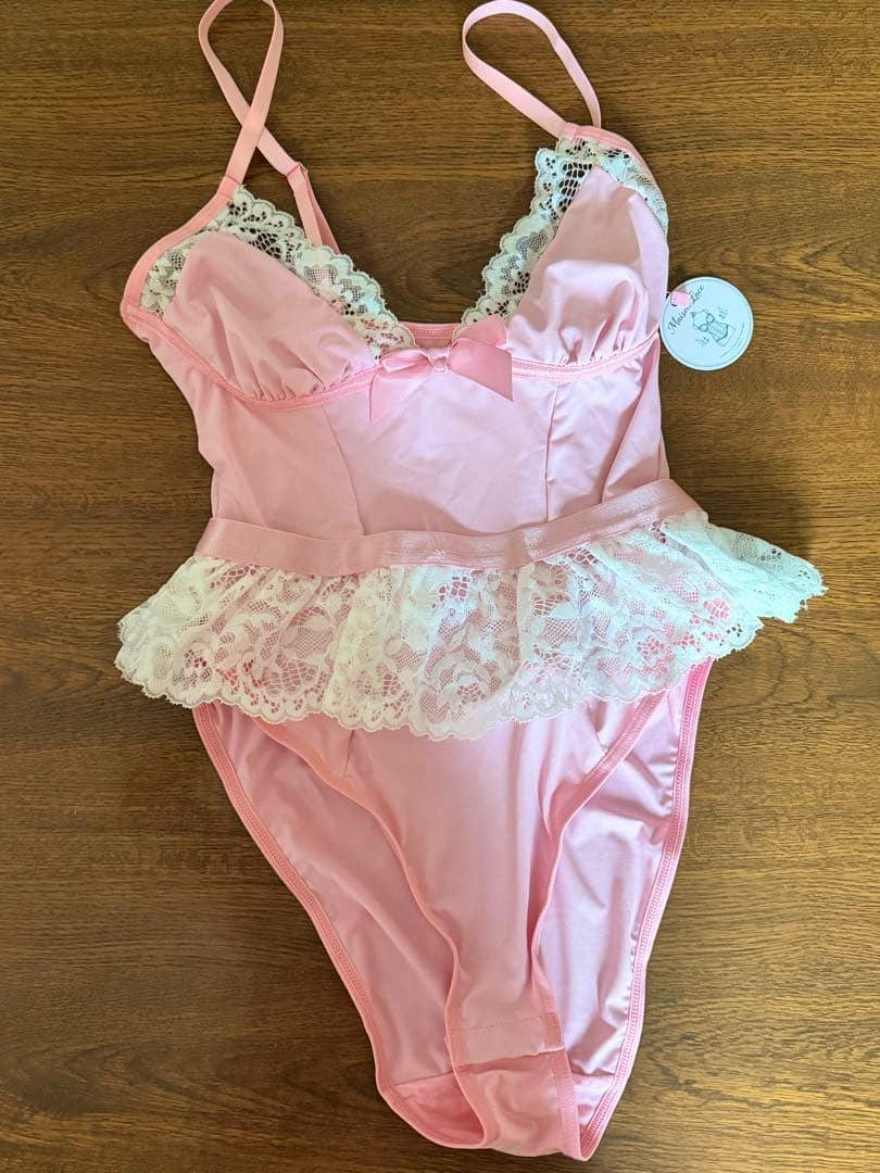 Pink lingerie bodysuit with white lace frill and straps laid flat on a wooden surface.