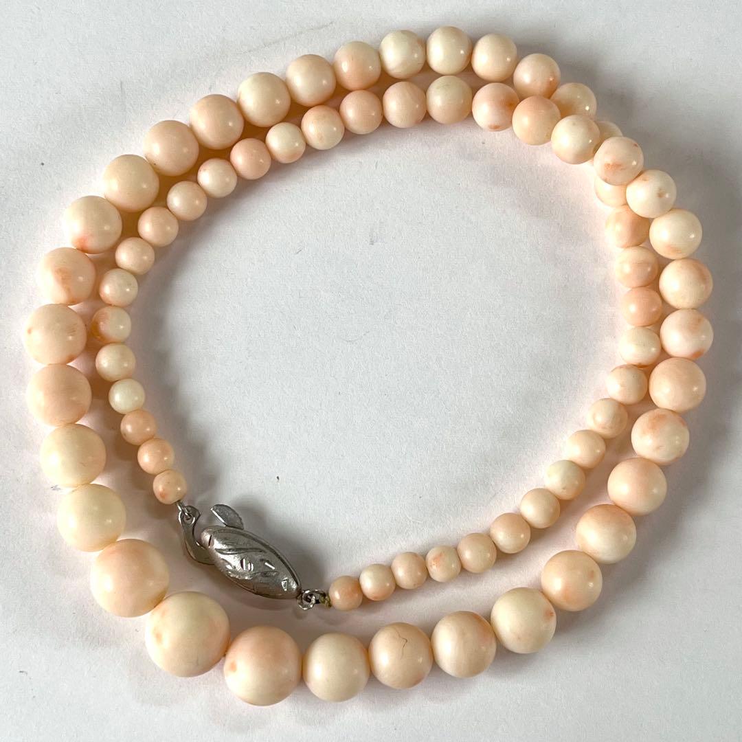 A graduated pink coral round-bead necklace with a silver clasp coiled on a white background.