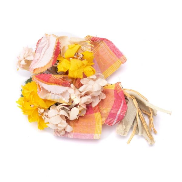 Multicolored checkered fabric flower brooch with yellow and pale petals and hanging ribbon tails on a white background.