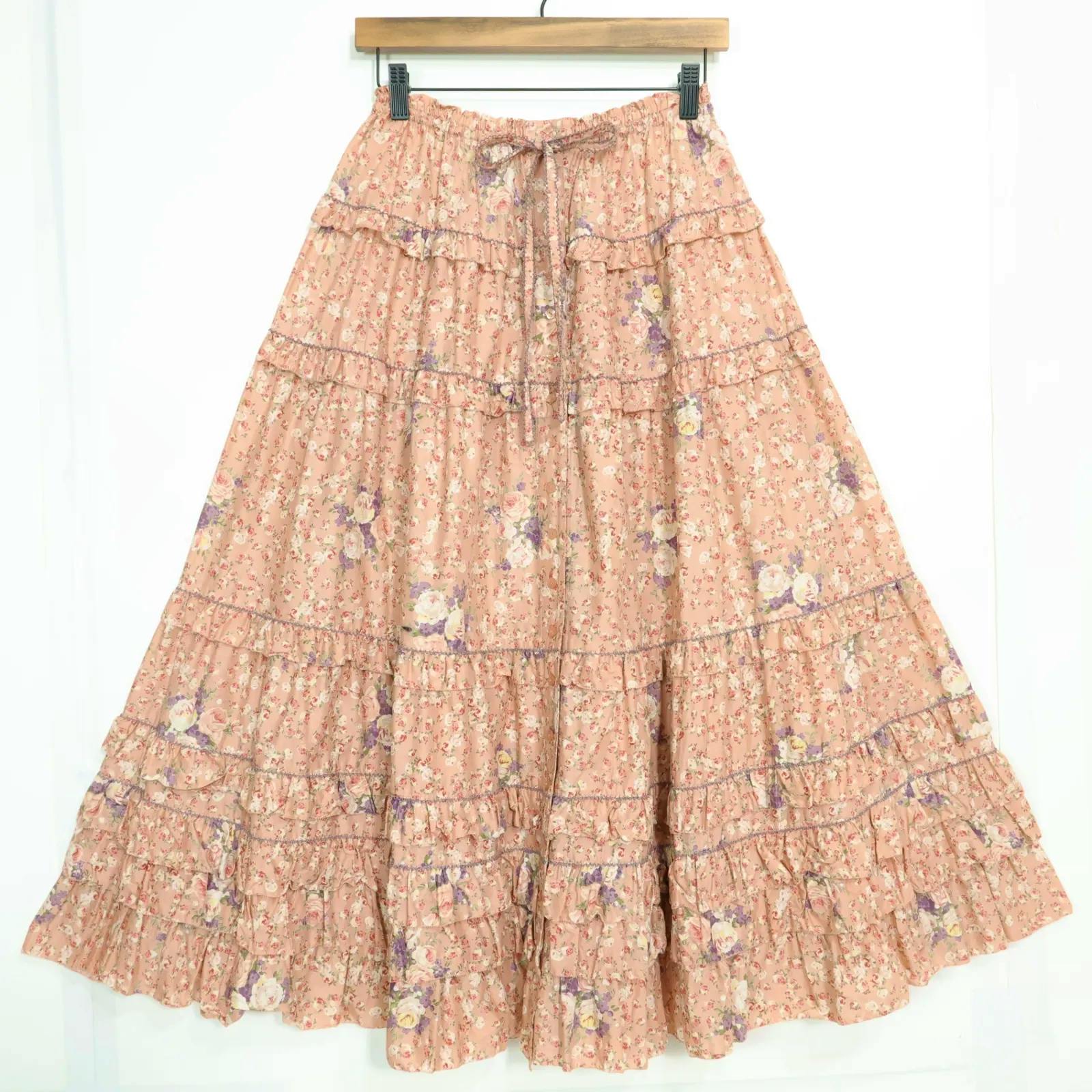 Salmon-pink floral gathered tiered skirt with ruffled tiers and a front tie hanging on a wooden hanger.