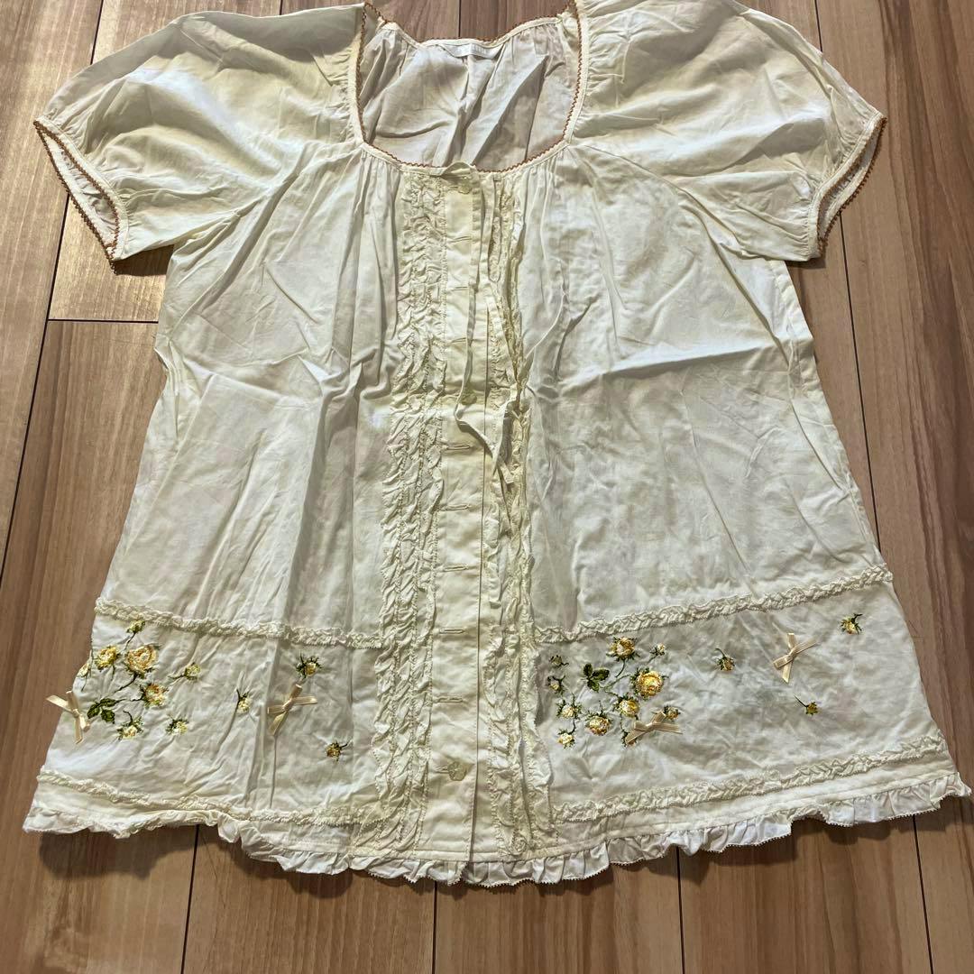White short-sleeve blouse with floral embroidery laid flat on a wooden floor.