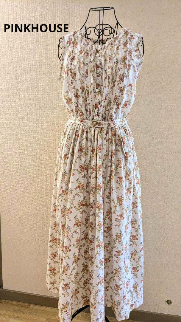 A women's polyester floral sleeveless belted vintage-style dress displayed on a wire dress form against a beige wall.