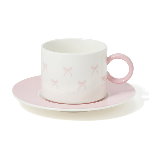 Porcelain cup with small pink ribbon motifs and a matching pink saucer on a white background.