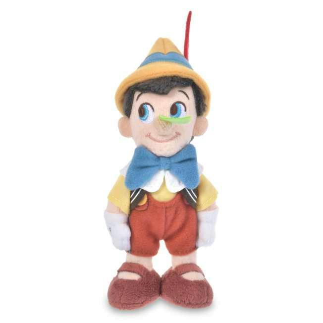 Front view of a Pinocchio plush toy standing against a white background, wearing a yellow hat with a red feather, blue bow, yellow shirt, red shorts, white gloves, and brown shoes.