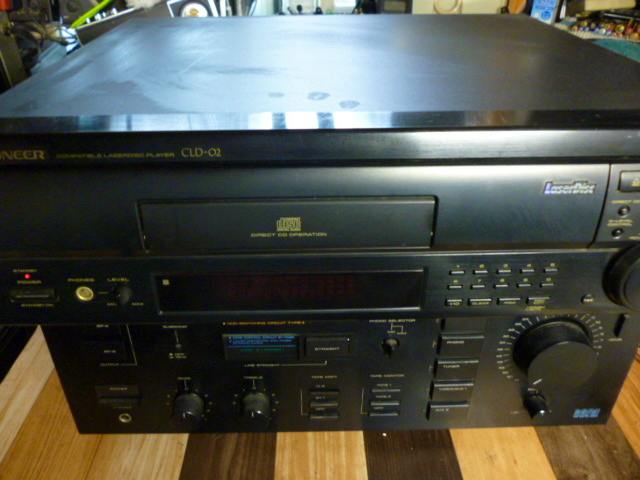 Front and top view of a Pioneer CLD-02 LaserDisc player showing the disc tray, display, and control knobs.