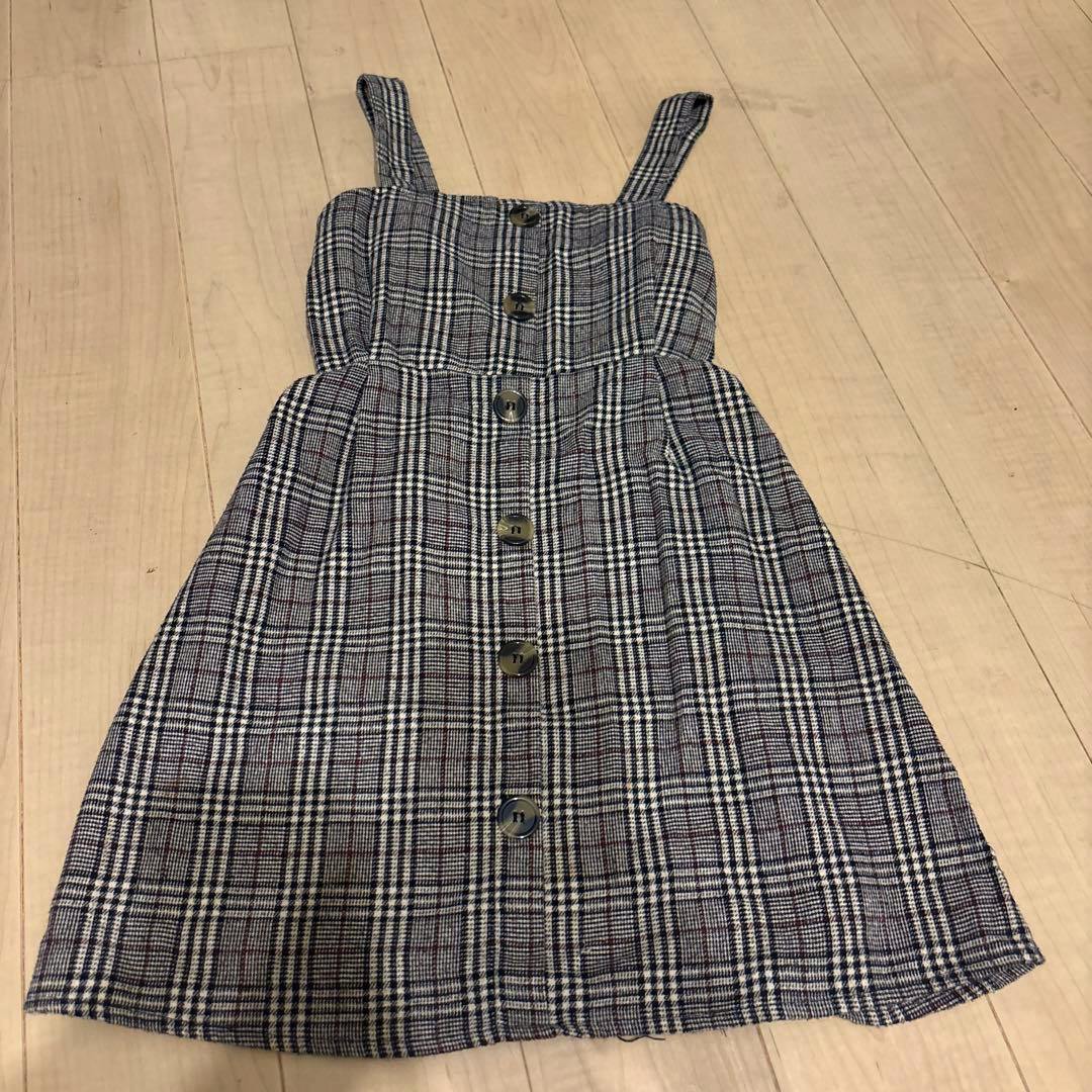 Plaid jumper skirt with front buttons and shoulder straps laid flat on a wooden floor.