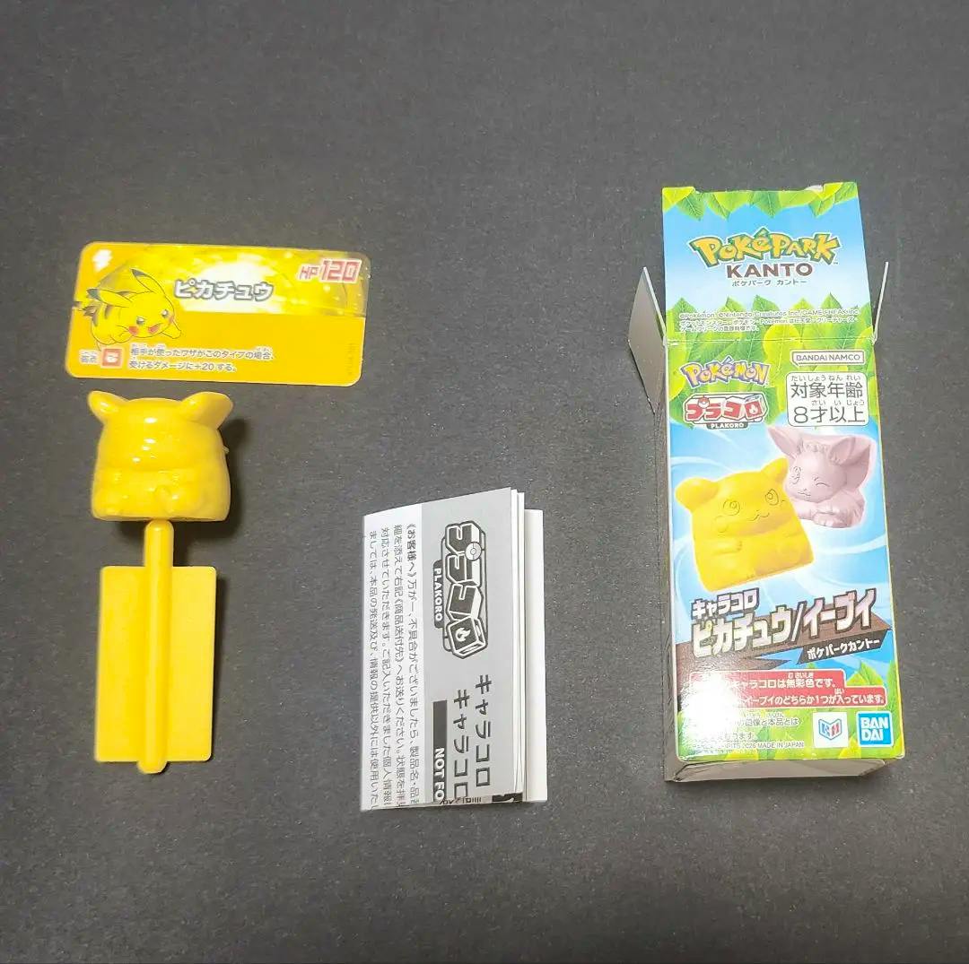 A yellow plastic Pikachu toy with its box, a small character card, and an instruction leaflet on a dark surface.