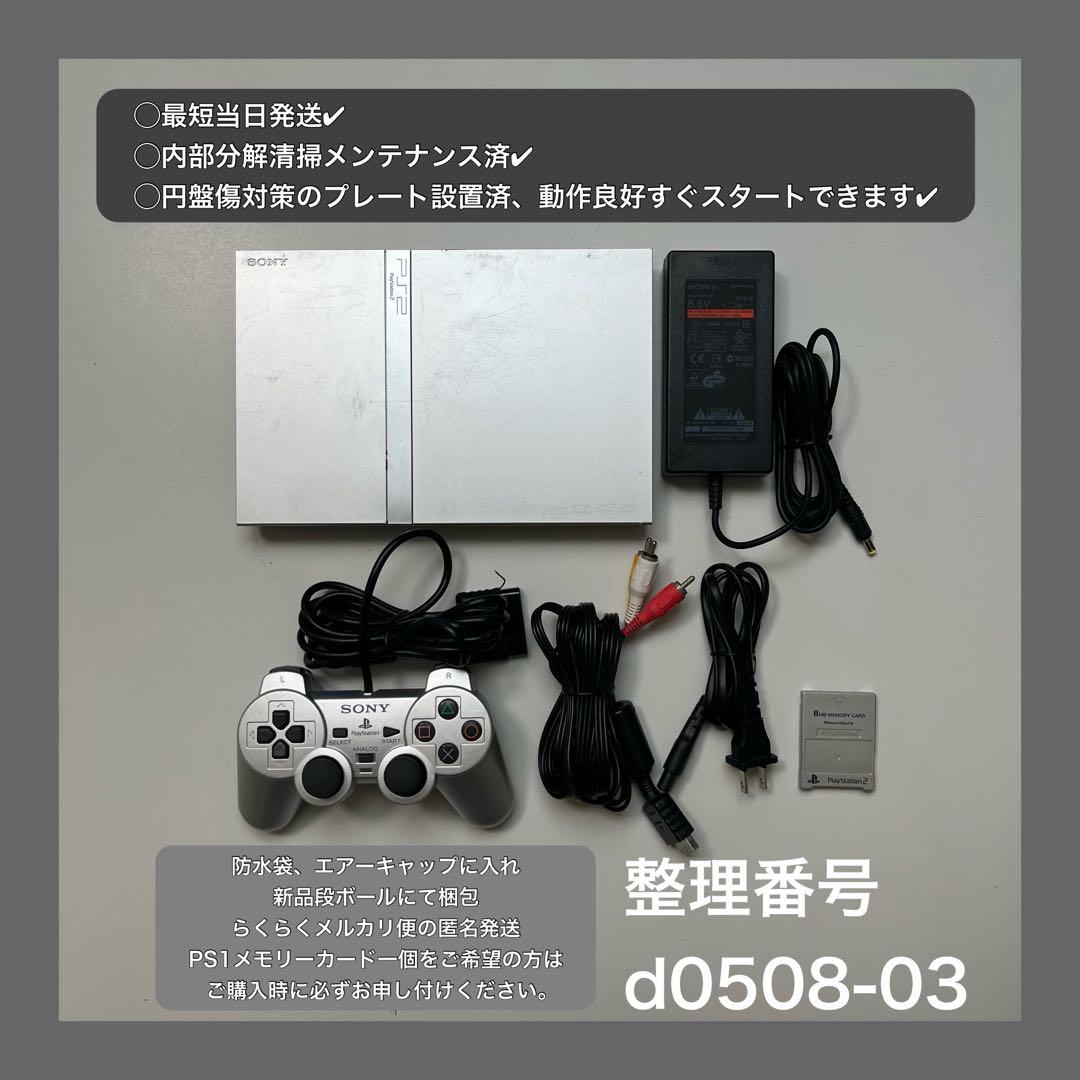 Overhead photo of a silver PlayStation 2 slim console with a Sony controller, power adapter, AV cables, and a memory card arranged on a light surface.