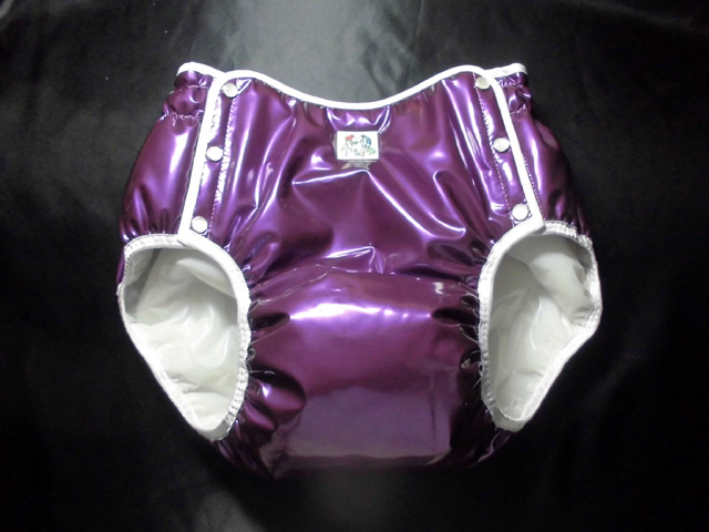 Purple glossy diaper-cover panty with white elasticized leg openings and snap closures laid flat on a dark background.